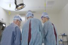 Three people in medical scrubs stand over an operating table. 